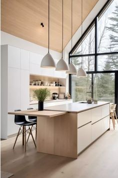 a kitchen with wooden floors and white walls, along with large windows that look out onto the woods