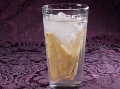 a glass filled with ice and lemon wedges on top of a purple table cloth