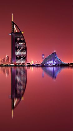 the burj building is lit up at night with its reflection in the water