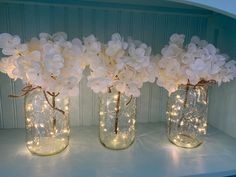 three mason jars filled with white flowers and fairy lights are sitting on a shelf next to each other