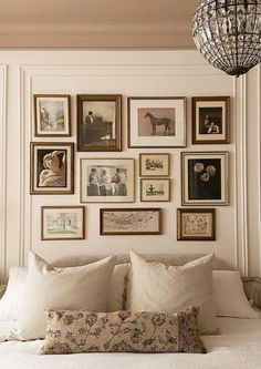 a white bed topped with lots of pillows and framed pictures on the wall above it