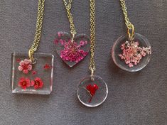 three glass pendants with flowers in them on a gray surface and one has a gold chain