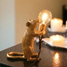 a lamp with a rat holding a light bulb on it's side sitting on a table