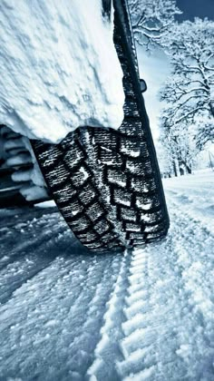 the tire of a car covered in snow on a snowy road with trees behind it