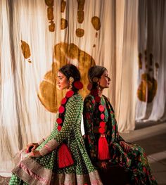 two women sitting on the ground in colorful dresses with red and green tassels