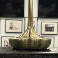 a golden clock sitting on top of a wooden table in front of framed pictures behind it