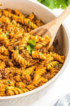 a wooden spoon in a pot full of pasta and meat sauce with parsley on the side