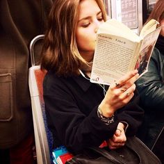 a woman reading a book while sitting in a chair on a train, with her eyes closed