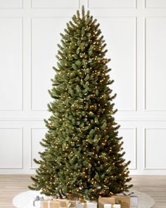 a christmas tree with presents under it on a wooden floor in front of a white wall