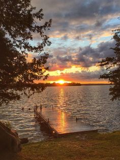 the sun is setting over the water and people are on the dock in the distance