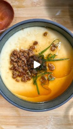 a bowl of soup with meat and vegetables in it next to a spoon on a wooden table