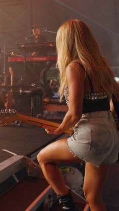 a woman standing on top of a stage with a guitar in her hand and another person behind her