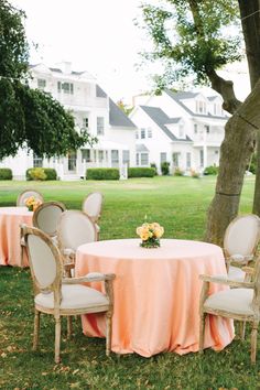 an outdoor table set up with pink linens and white chairs in front of a large house