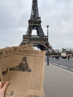 someone is holding up an old newspaper in front of the eiffel tower, paris