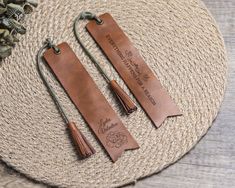 two personalized leather bookmarks with tassels on a woven place mat next to flowers