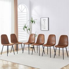 six brown chairs sitting on top of a wooden floor next to a plant in a white room