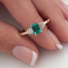 a woman's hand holding a ring with an emerald and two baguettes