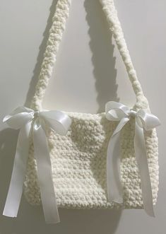 a crocheted purse with white ribbon and bows on the front, hanging from a hook