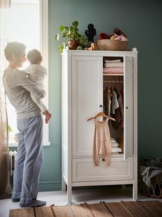 a woman holding a baby in her arms next to a white cabinet with clothes on it