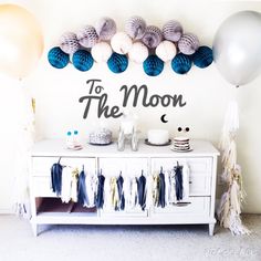 a table with balloons, cake and decorations on it in front of a wall that says to the moon