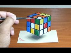 someone is drawing a rubik cube with colored pencils on a piece of paper