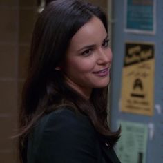 a woman standing in front of a locker with signs on the wall behind her and smiling