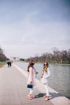 two girls standing on the edge of a walkway next to a body of water in front of the lincoln memorial