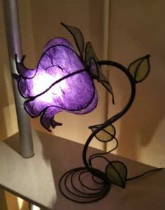 a purple flower lamp sitting on top of a table next to a white wall and floor