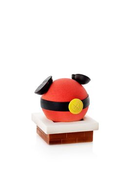 a red ball with black ears on top of a white base and a yellow button