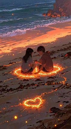 two people sitting on the beach next to each other with hearts drawn in sand at night