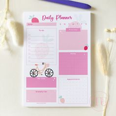 a pink planner with a bike on it and flowers next to it, along with a blue pen