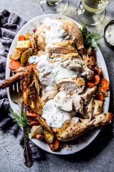 a white plate topped with chicken, potatoes and carrots next to two wine glasses