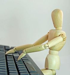 a wooden toy sitting on top of a laptop computer keyboard with its arms and legs crossed