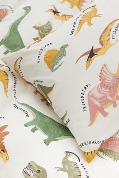 two pillows with dinosaurs on them sitting next to each other in front of a pillow case