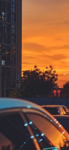 the sun is setting behind some tall buildings and cars in front of it, with an orange sky