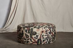 a round ottoman sitting on top of a floor next to a white wall and curtain