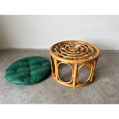 a round bamboo table with a green cushion on the floor and a white wall in the background