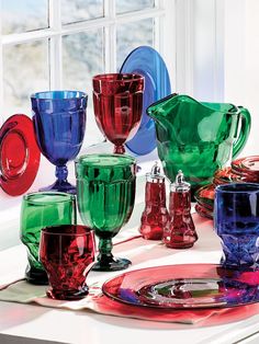 there are many different colored glassware on the counter top in front of a window