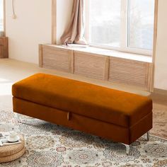 an orange bench sitting on top of a rug in front of a window with curtains