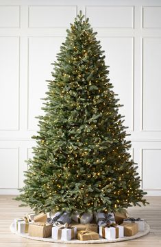 a christmas tree with presents under it on a wooden floor in front of a white wall