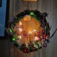 a wreath made out of flowers and mushrooms hanging on a wall with a light in the middle