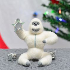 a white stuffed animal sitting on top of a table next to a christmas tree and presents