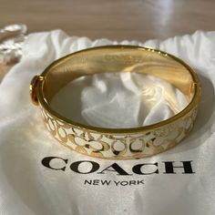 a gold coach bracelet sitting on top of a white cloth