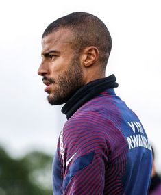 a close up of a person wearing a jacket and standing with trees in the background