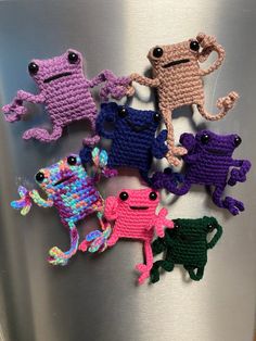 six crocheted frogs sitting on top of a stainless steel refrigerator with black eyes