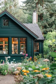 a small green house surrounded by flowers and trees