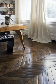 a wooden table sitting in front of a window next to a book shelf filled with books