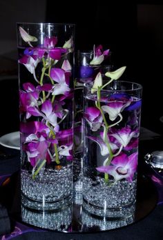 two vases filled with purple flowers on top of a black tablecloth covered table