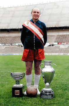 a man standing on top of a soccer field next to trophy cups and an award