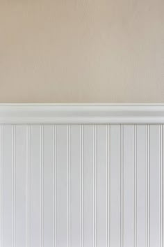 a cat sitting on top of a wooden bench in front of a white paneled wall